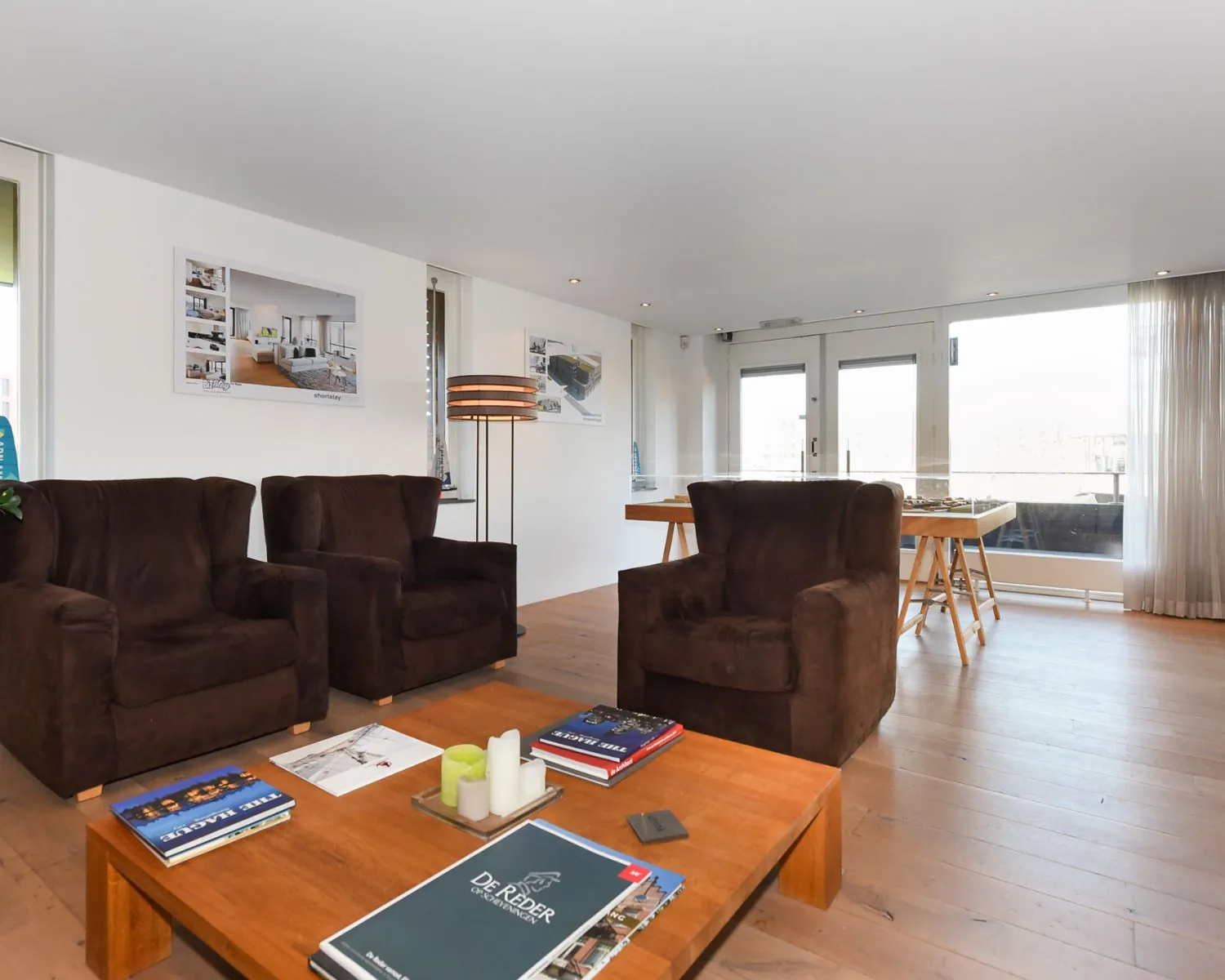 Modern ingerichte woonkamer met donkerbruine fauteuils, houten vloer en grote raampartijen aan de Dr. Lelykade 257 in Den Haag.