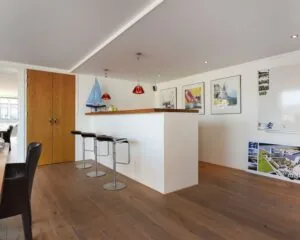 Moderne kantoorruimte met houten vloer, een witte bar met drie barkrukken, en zeilthema-decoratie aan de muur in Dr. Lelykade 257 te Den Haag.