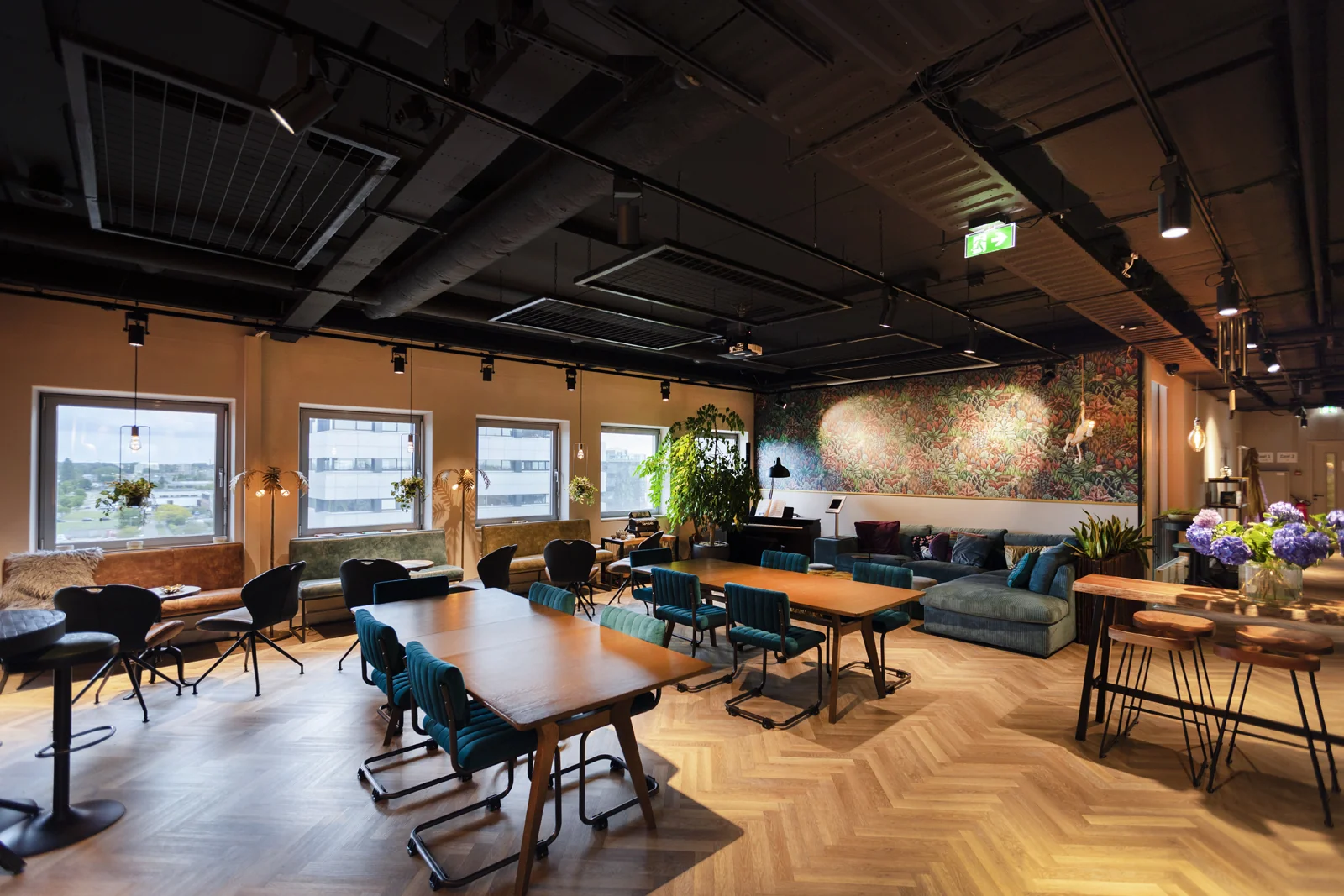 Moderne, sfeervolle foyer van de academie met houten vloer, kleurrijk meubilair en een artistieke muurdecoratie.