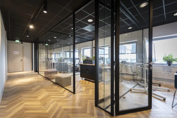 Modern kantoorinterieur van de Academie met glazen vergaderruimtes en visgraat houten vloer.