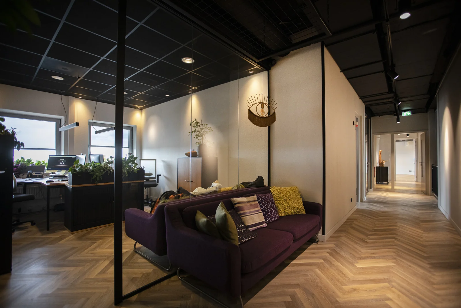 Moderne kantoorruimte van de Academie met paarse bank, glazen vergaderruimte en houten visgraatvloer.
