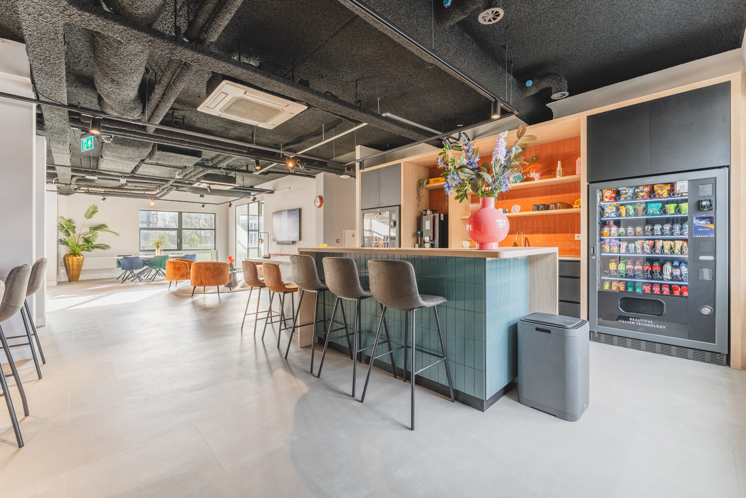 Moderne en lichte lounge- en keukenruimte met bar, barkrukken, frisdrankautomaat en zithoek bij Adress_3.