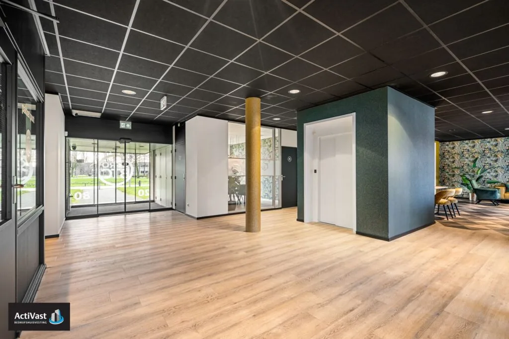 Moderne entreehal van het kantoorpand Agro Business Park 22 met glazen schuifdeuren, lift en zithoek.