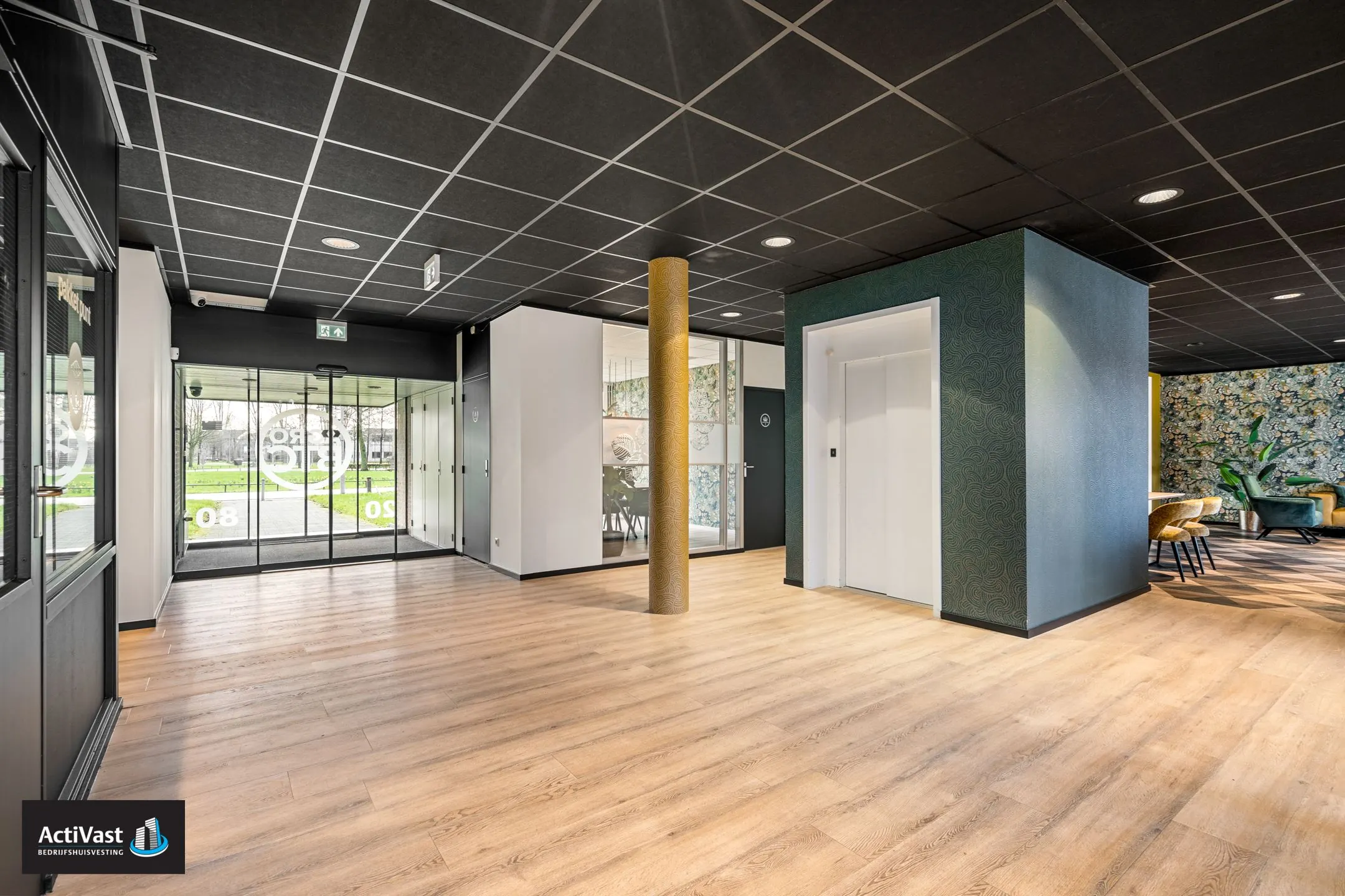 Moderne entreehal van het kantoorpand Agro Business Park 22 met glazen schuifdeuren, lift en zithoek.