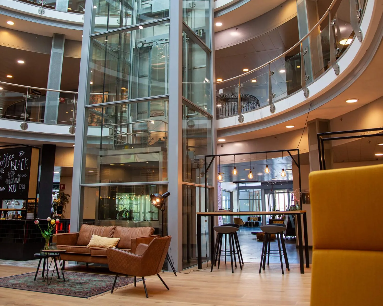 Moderne en open kantoorlobby in Almere met glazen lift, zithoek en hoge werktafels.