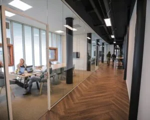 Mensen zitten te vergaderen in een glazen vergaderruimte langs een moderne kantoorhal in Amsterdam-Amersfoort.