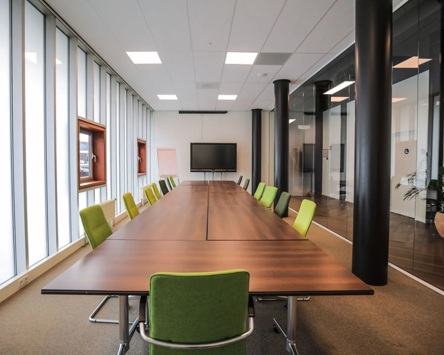 Moderne vergaderruimte in Amsterdam-Amersfoort met lange houten tafel, groene stoelen en een presentatiescherm.