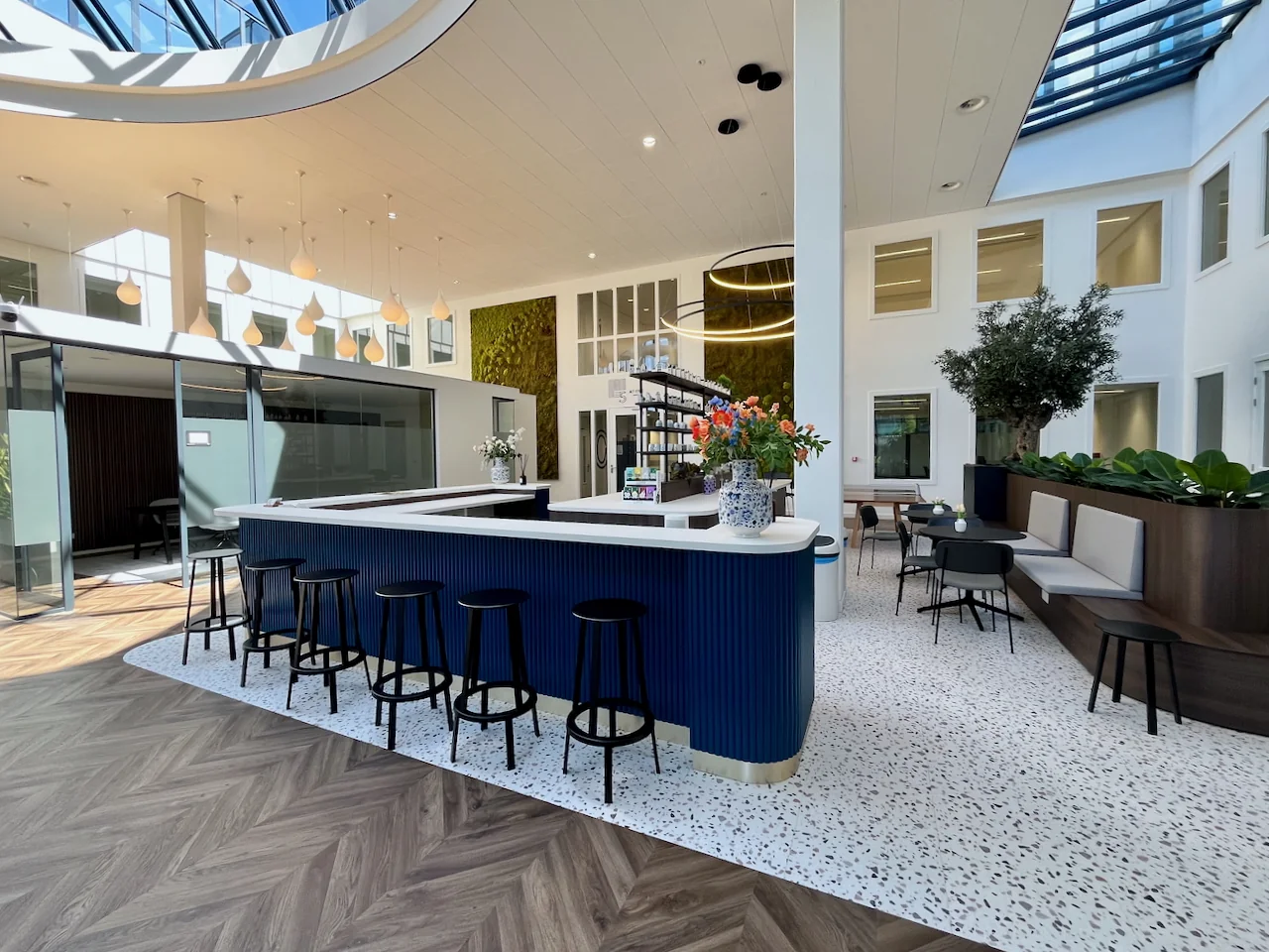 Moderne lounge genaamd Lounge 0.11 met een centraal barmeubel, zitgedeelte en veel natuurlijk licht.