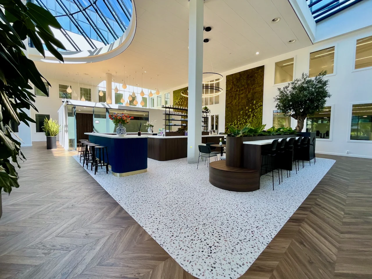 Moderne lounge 0.12 met een centrale bar, groene accenten en veel natuurlijk licht dankzij een groot glazen plafond.