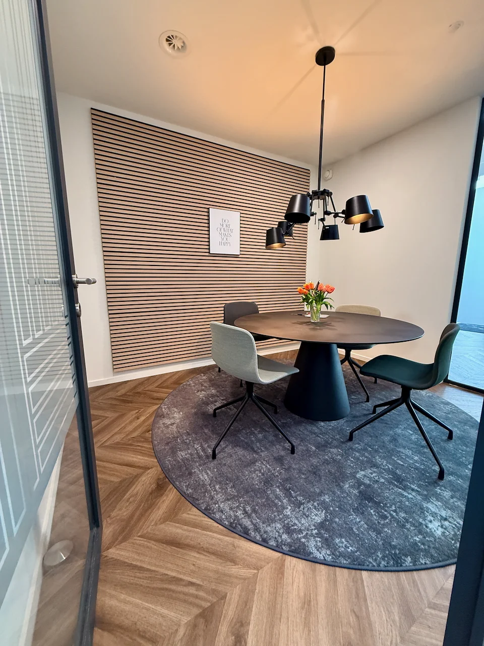 Moderne vergaderruimte met ronde tafel, vier stoelen, een hanglamp en een bloemenvaas op een rond vloerkleed.