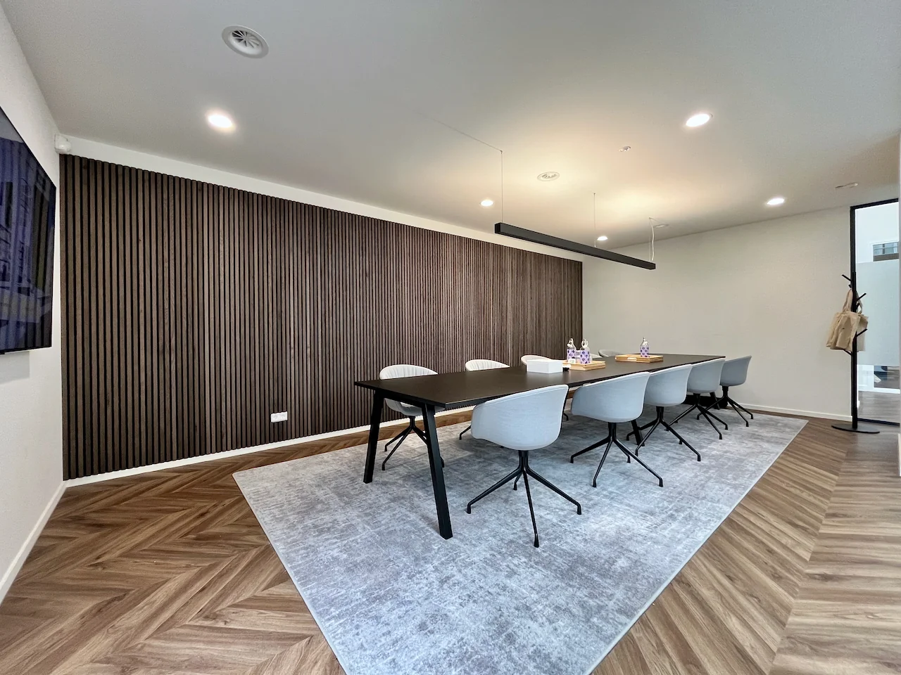 Moderne vergaderruimte met een lange tafel, acht stoelen en een houten wandpaneel.