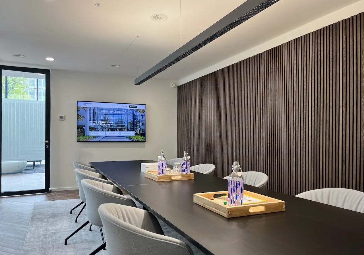 Moderne vergaderruimte met lange zwarte tafel, comfortabele stoelen en een scherm aan de muur.