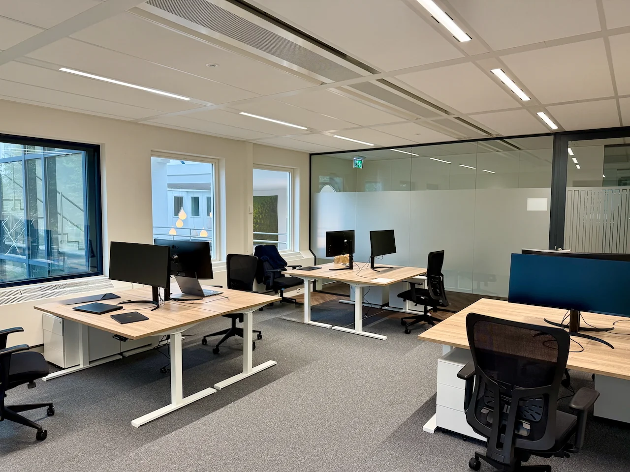 Moderne, open kantoorruimte bij At Five Offices met meerdere bureaus, bureaustoelen en computerschermen.