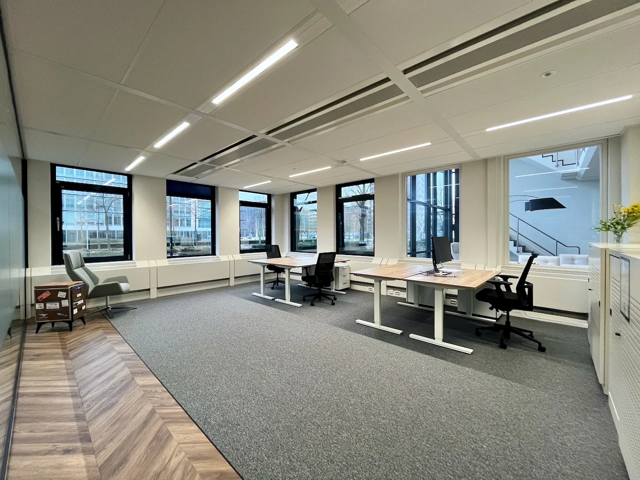 Moderne kantoorruimte met grote ramen, verstelbare bureaus en ergonomische bureaustoelen.