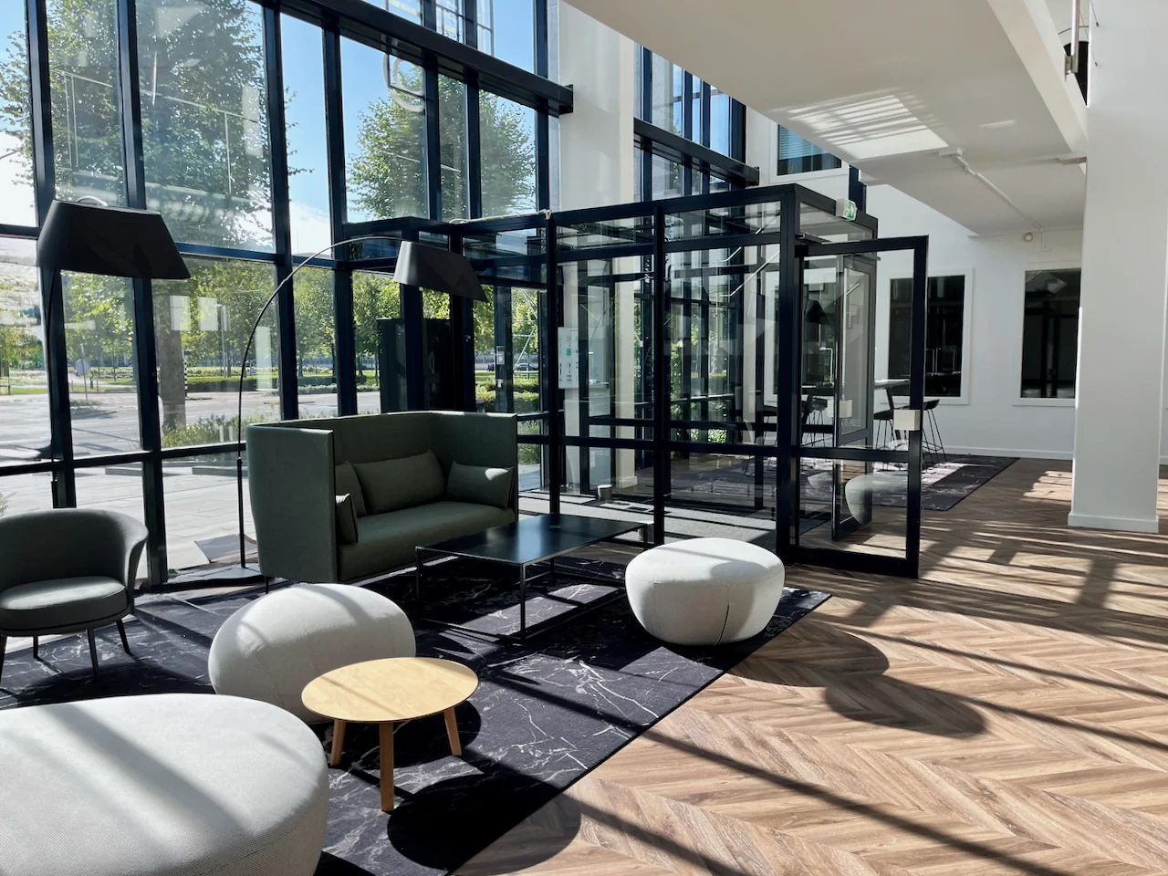 Moderne loungehoek genaamd Lounge 0.04 met designmeubels, veel daglicht en glazen wanden in een stijlvolle kantoorruimte.