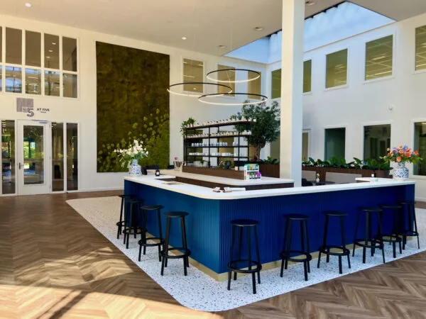 Moderne lounge genaamd Lounge 0.07 met een blauwe bar, hoge krukken, groene wanddecoratie en veel natuurlijk licht.