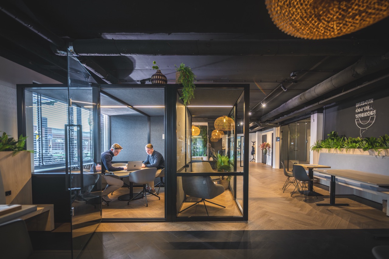 Twee mannen werken samen aan een tafel in een moderne glazen vergaderruimte binnen het BOW-kantoor.