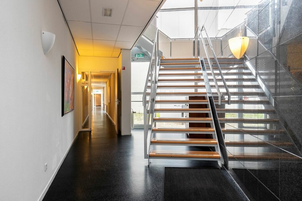 Moderne hal met een open houten trap en een verlichte gang in het gebouw aan de Banningstraat 3.