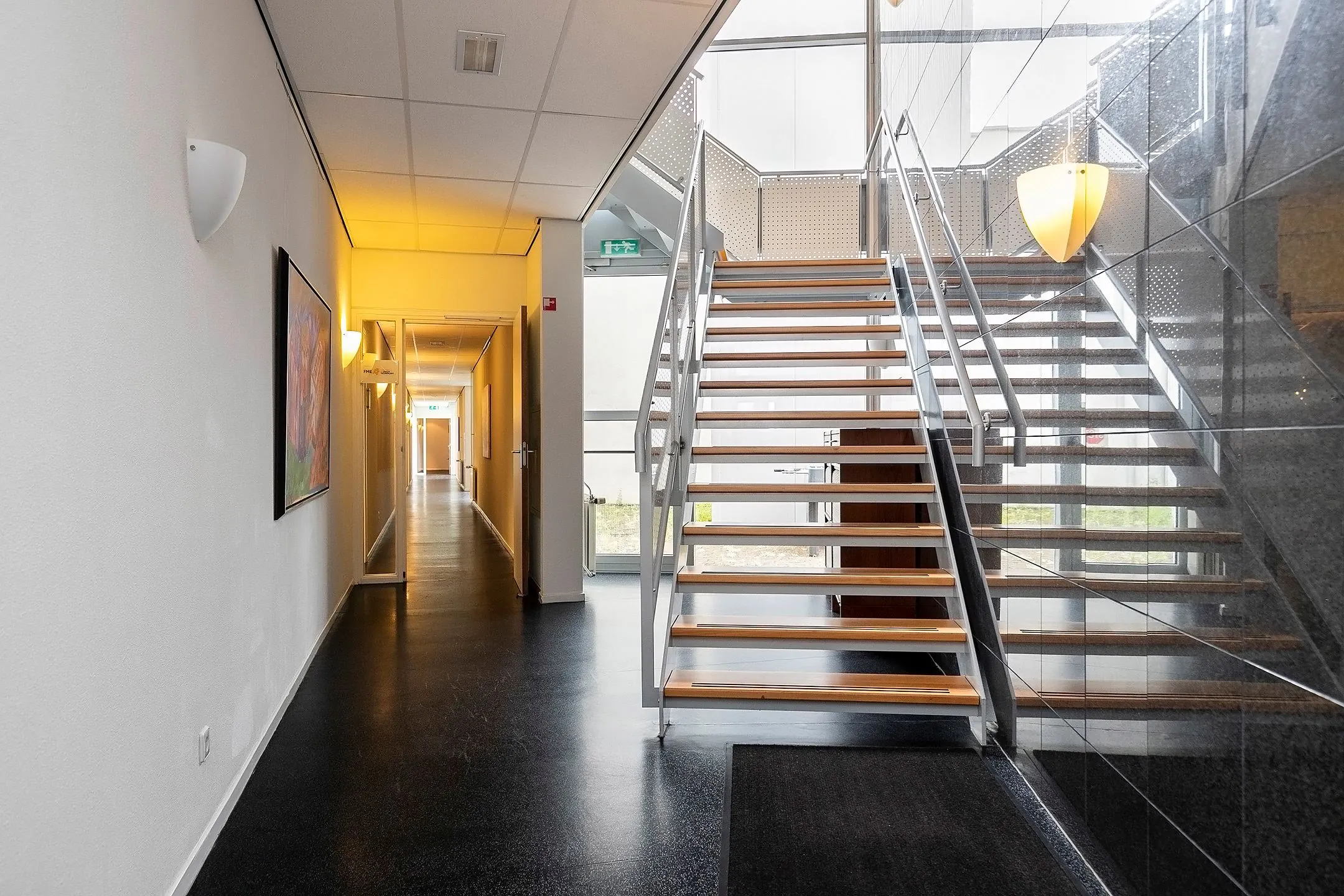 Moderne hal met een open houten trap en een verlichte gang in het gebouw aan de Banningstraat 3.