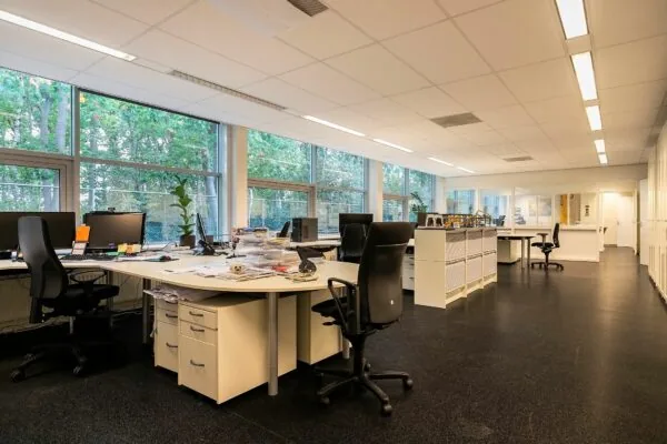 Modern kantoorinterieur aan de Banningstraat 3-5 met bureaus, computers en grote ramen met uitzicht op bomen.