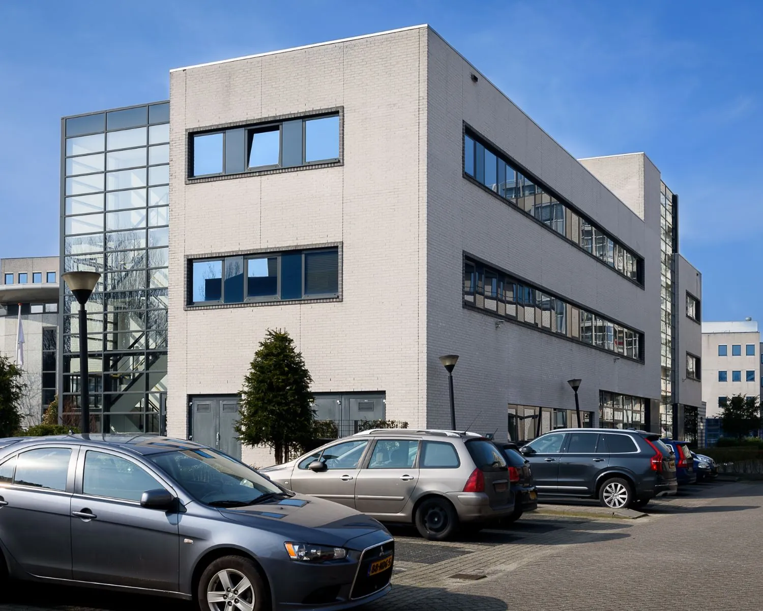 Modern kantoorgebouw aan de Barbizonlaan 55 in Capelle aan den IJssel met geparkeerde auto's op de voorgrond.