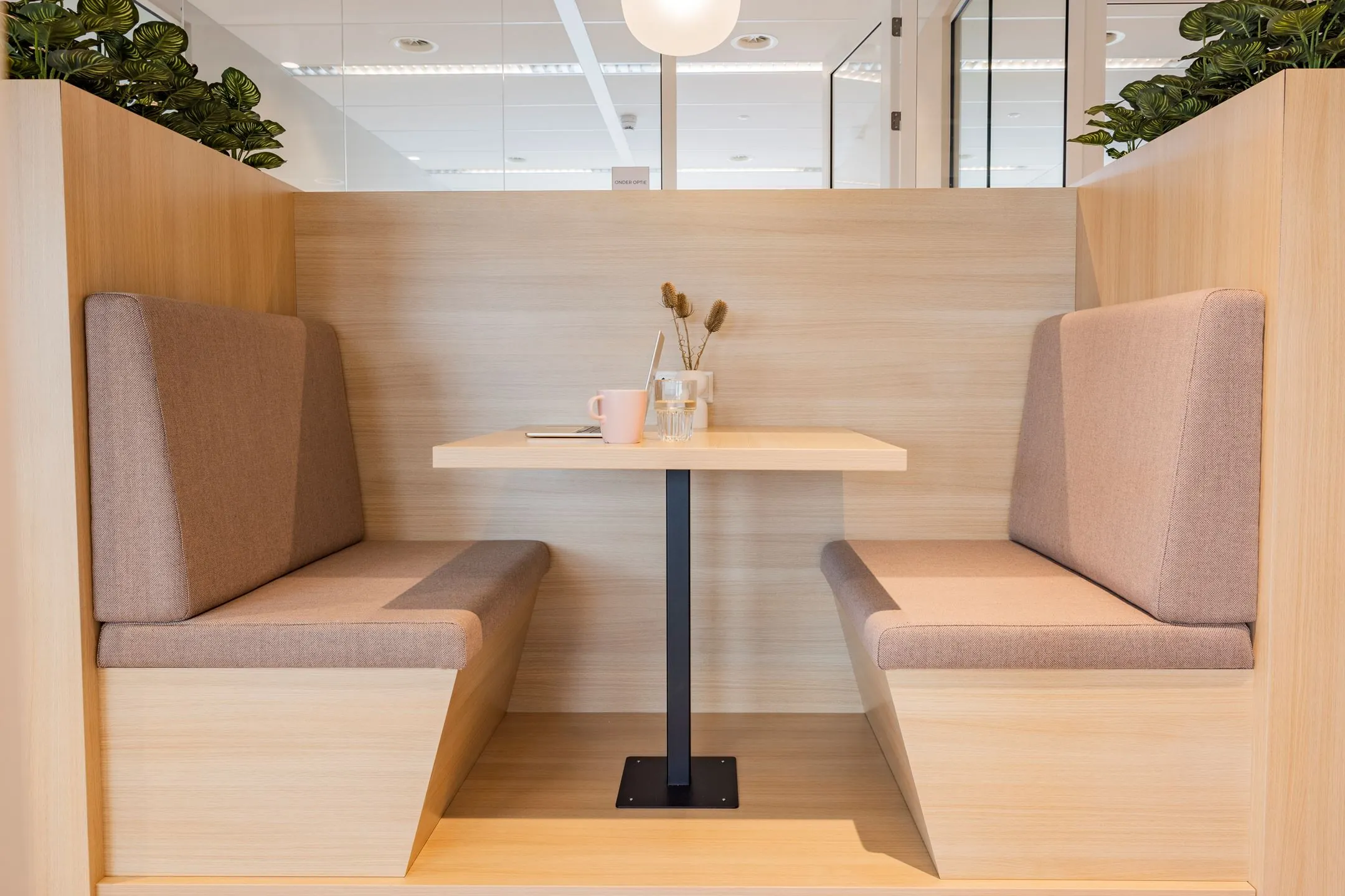 Moderne houten zithoek met zachte kussens, een tafel en decoratie in een kantoorruimte aan de Baron van Nagellstraat.