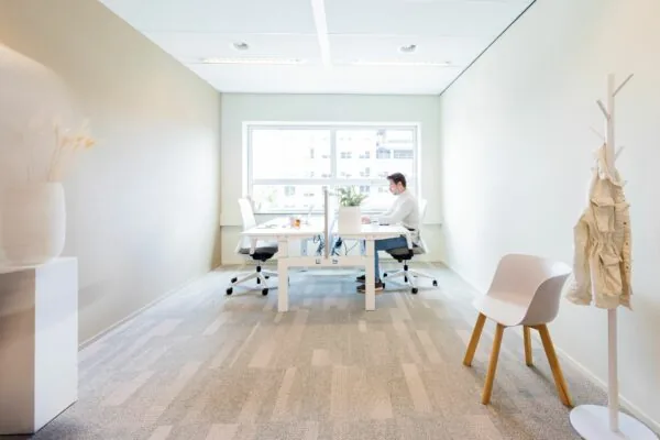 Moderne, licht ingerichte kantoorruimte aan de Baron van Nagellstraat 136 met twee werkplekken en een man die aan het werk is.