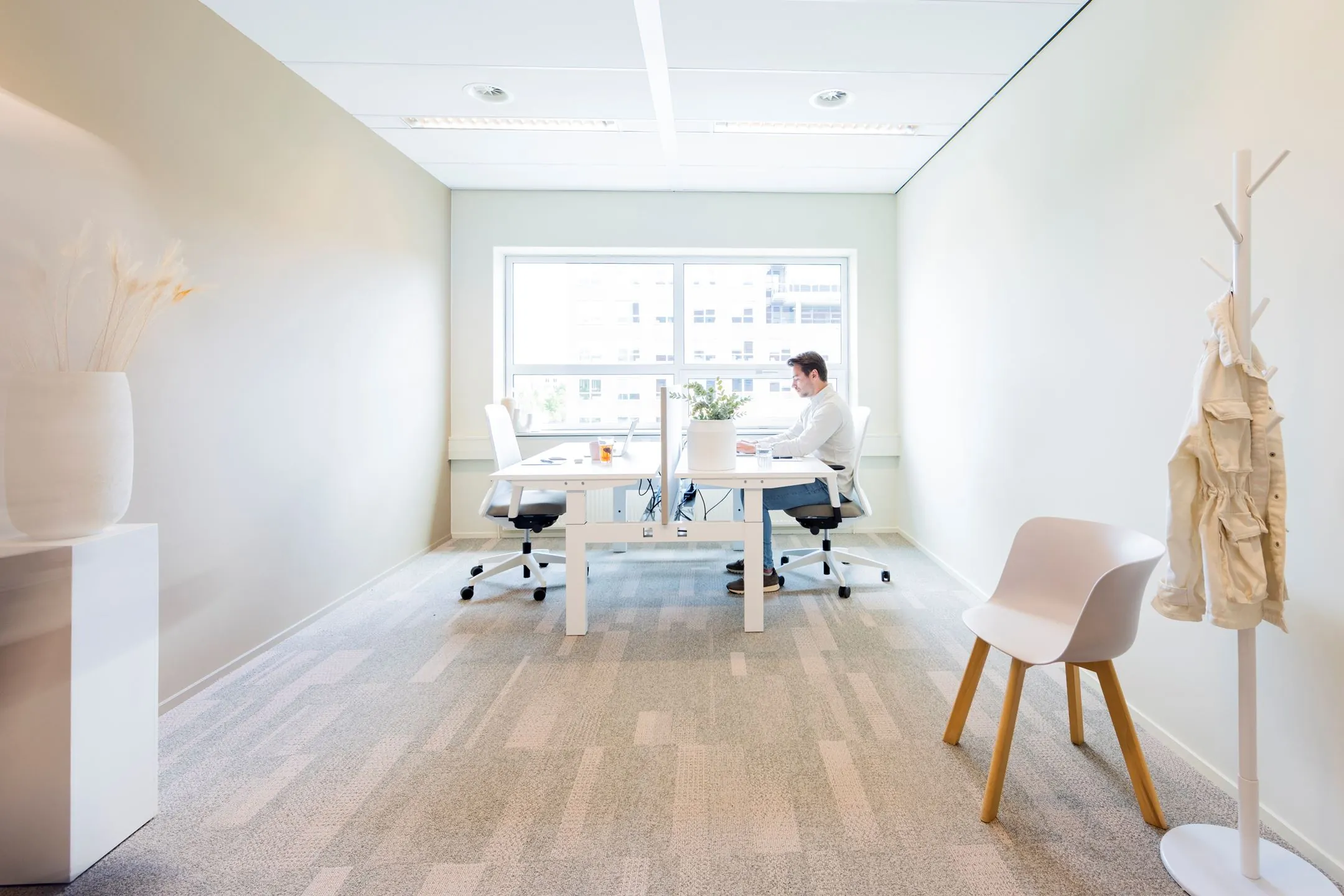 Moderne, licht ingerichte kantoorruimte aan de Baron van Nagellstraat 136 met twee werkplekken en een man die aan het werk is.