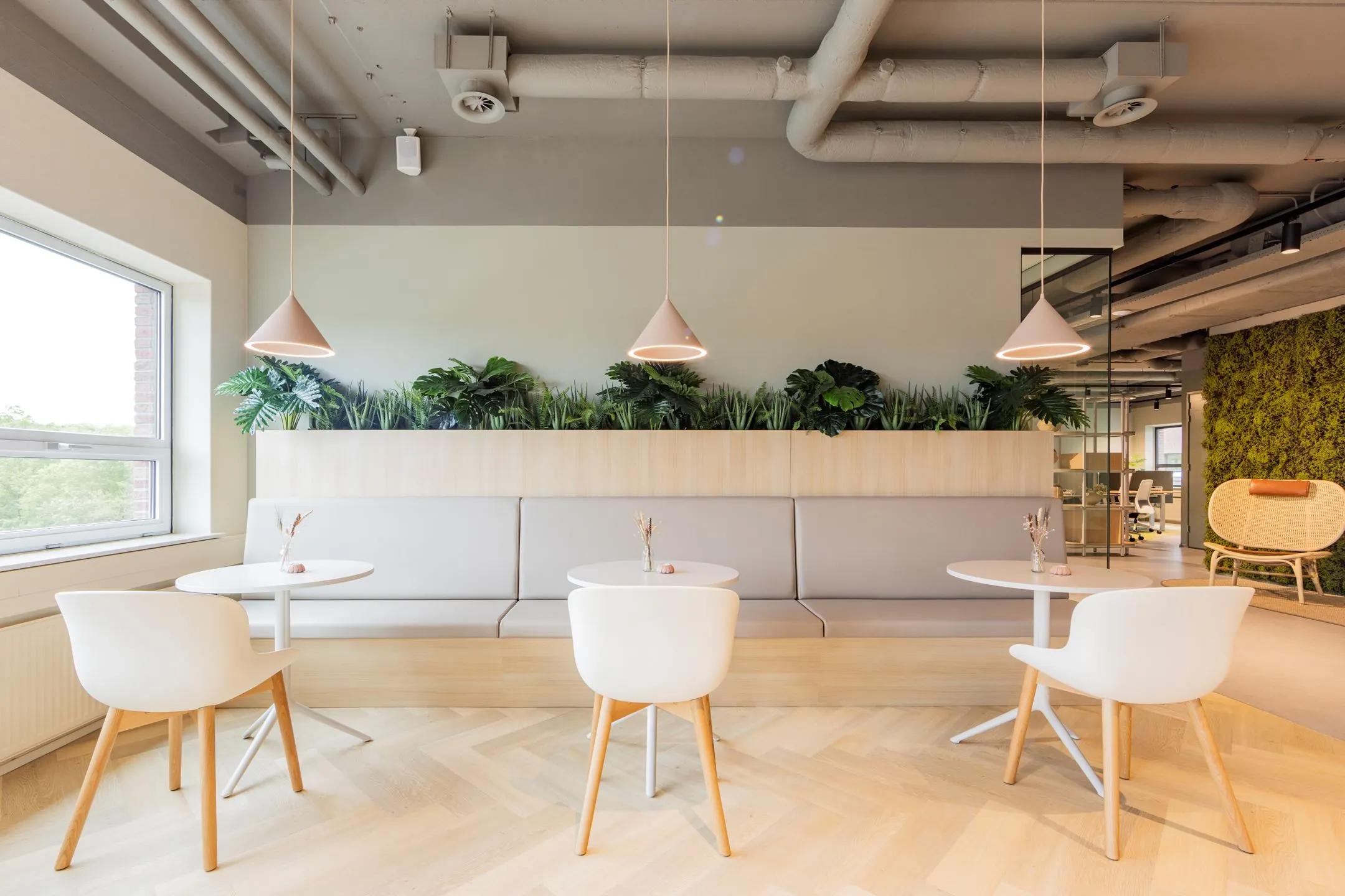 Moderne en licht ingerichte zithoek met witte stoelen, ronde tafels en groene planten in een kantoor aan de Baron van Nagellstraat 136.