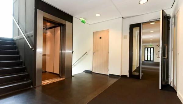 Hal met trap, open lift en meerdere deuren in kantoorgebouw aan de Bezuidenhoutseweg 161.