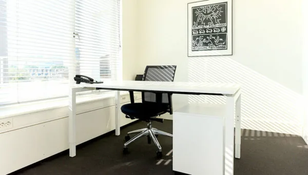 Lichte, moderne kantoorruimte aan de Bezuidenhoutseweg 161 met een wit bureau, zwarte bureaustoel en een kunstwerk aan de muur.
