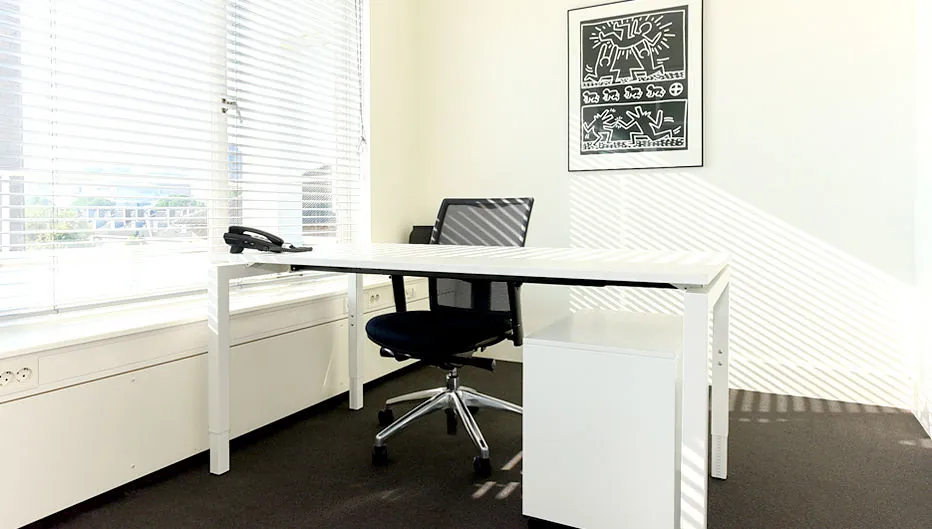 Lichte, moderne kantoorruimte aan de Bezuidenhoutseweg 161 met een wit bureau, zwarte bureaustoel en een kunstwerk aan de muur.