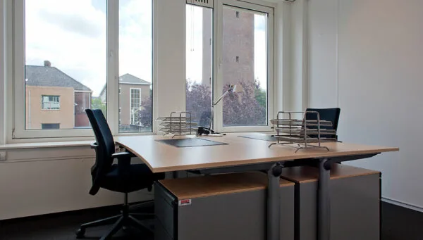 Modern kantoor met twee bureaus, bureaustoelen en uitzicht op gebouwen aan de Bezuidenhoutseweg.
