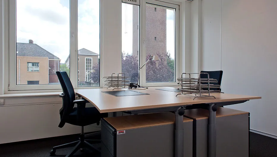Modern kantoor met twee bureaus, bureaustoelen en uitzicht op gebouwen aan de Bezuidenhoutseweg.