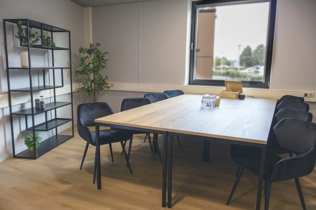 Vergaderruimte in Blankenstein 400 met houten tafel, zwarte stoelen, plantendecoratie en een groot raam.