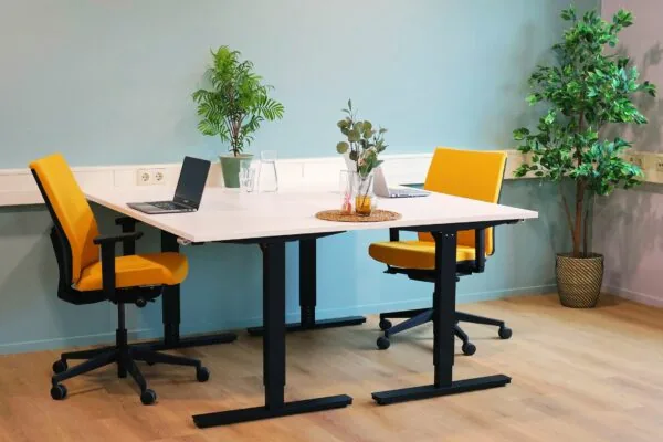 Moderne vergaderruimte in Blankenstein 400 met twee gele bureaustoelen, een witte tafel, laptops en groene kamerplanten.