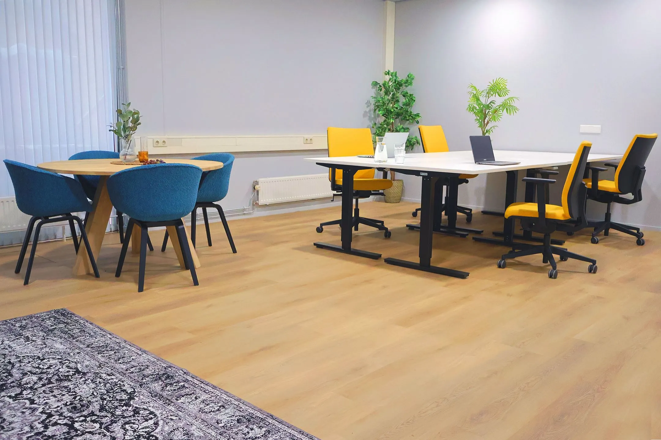 Moderne vergaderruimte in Blankenstein 400 met een ronde tafel en blauwe stoelen, naast een werktafel met gele bureaustoelen.