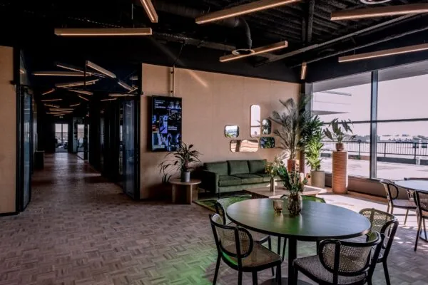 Moderne lounge- en werkruimte in Ceintuurbaan 28_1 met groene bank, ronde tafels, planten en grote ramen met uitzicht.