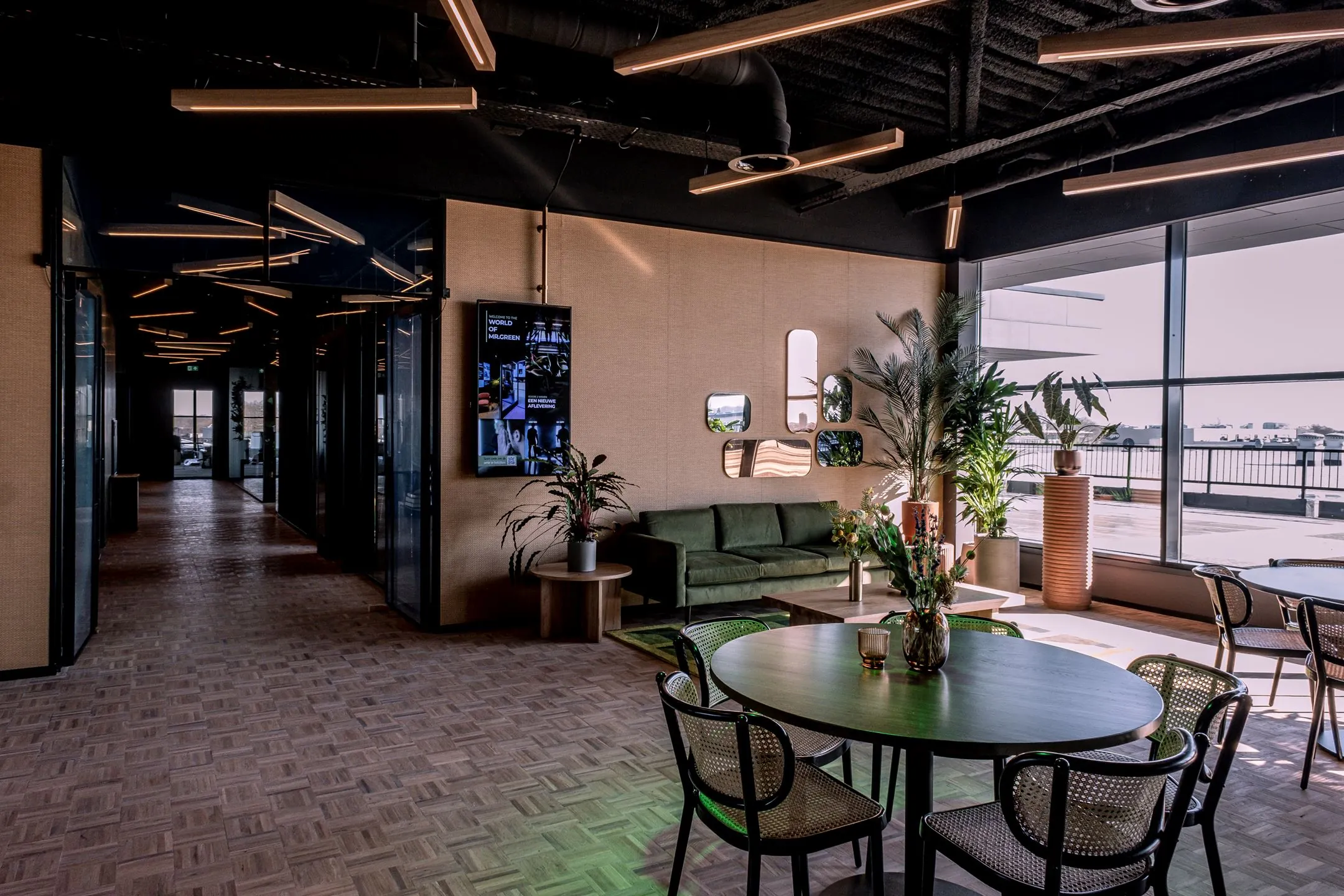 Moderne lounge- en werkruimte in Ceintuurbaan 28_1 met groene bank, ronde tafels, planten en grote ramen met uitzicht.