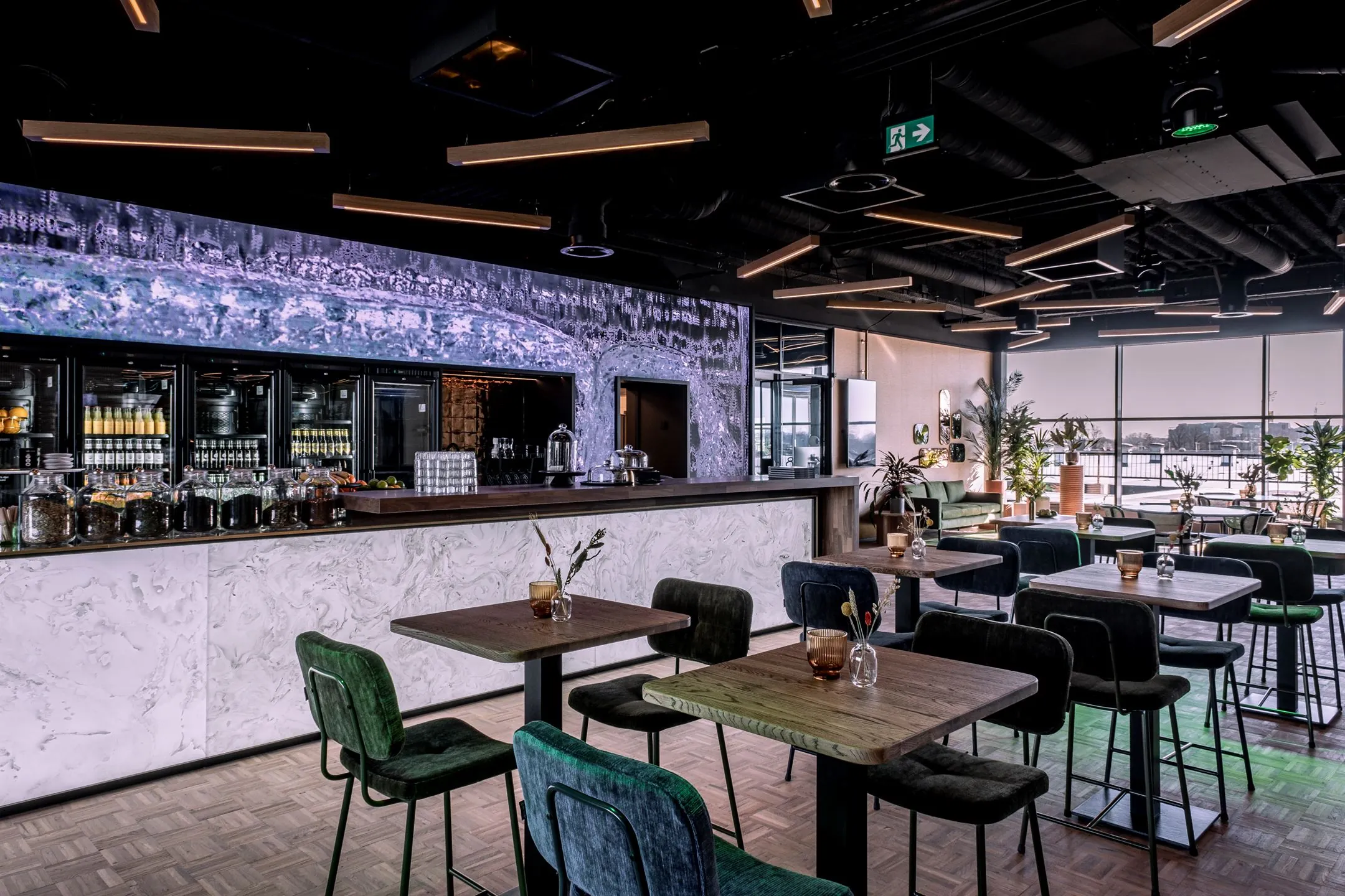 Modern ingerichte horecaruimte aan de Ceintuurbaan 28_10 met een marmeren bar, hoge tafels, fluwelen stoelen en grote ramen met uitzicht.