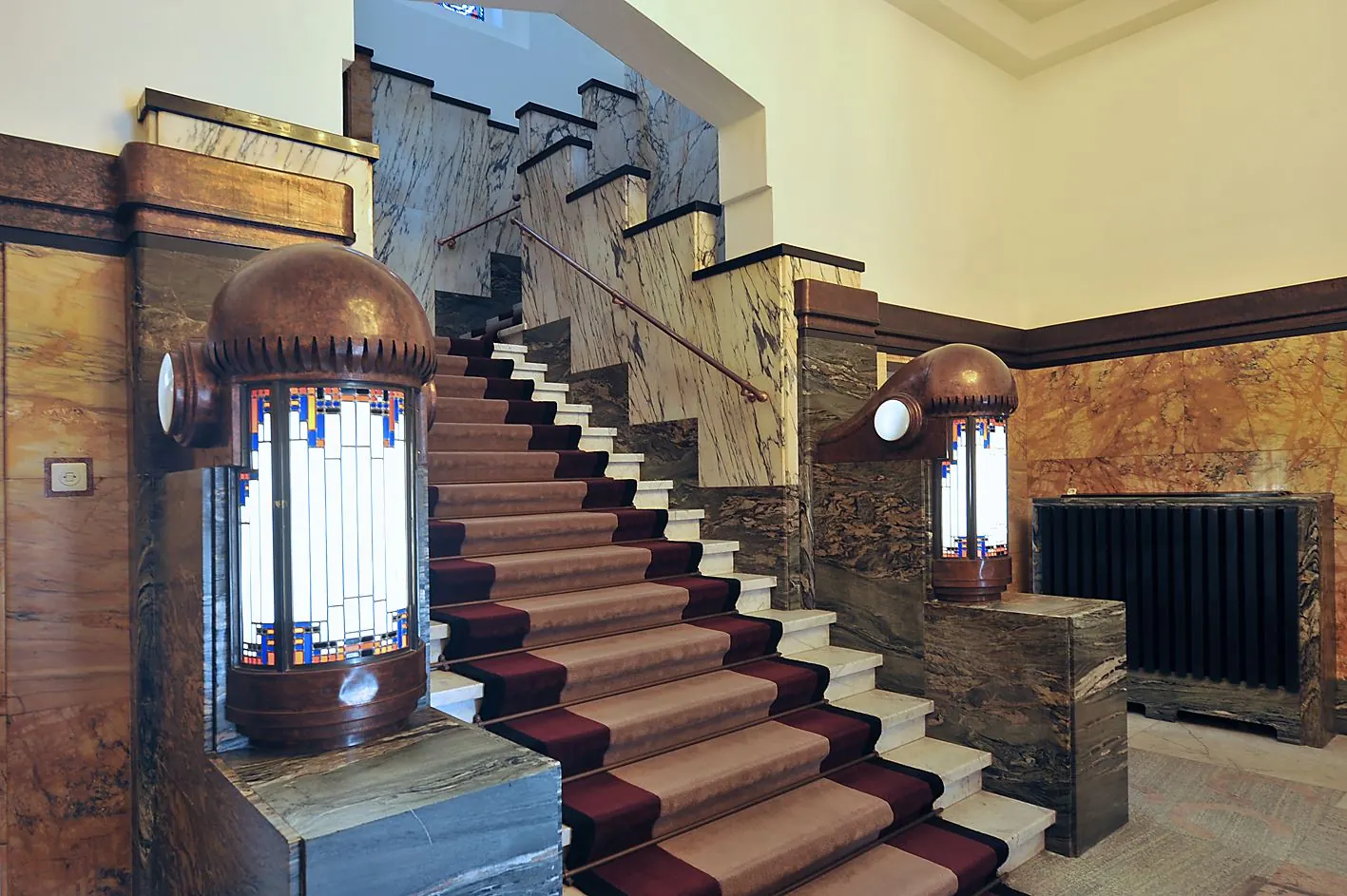 Monumentaal trappenhuis in art deco-stijl met marmeren wanden, rood tapijt en sierlijke lampen in Ceresstraat 13.