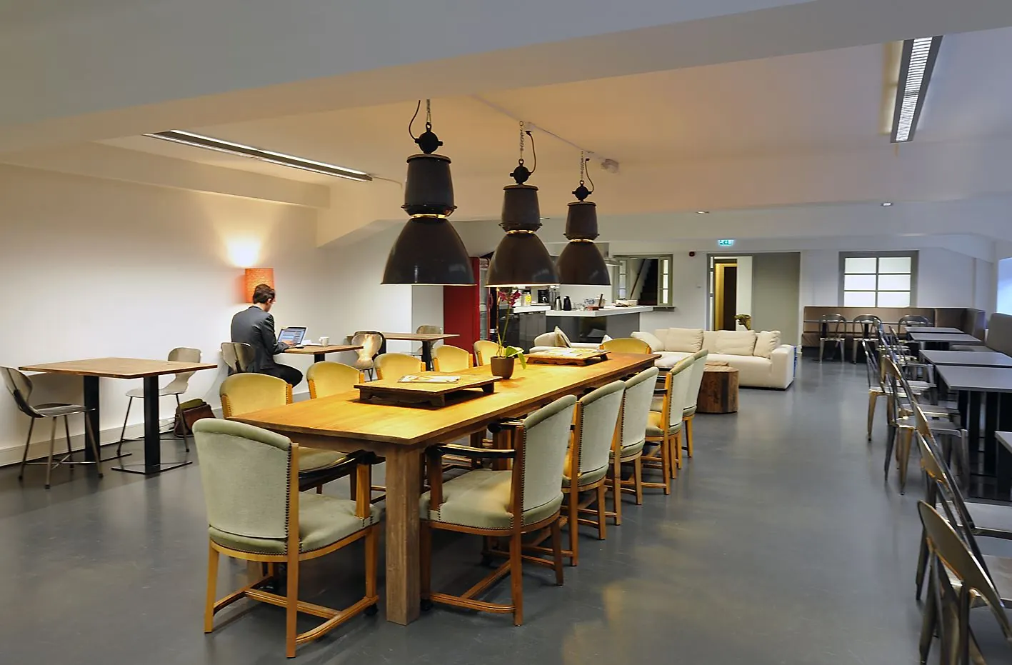 Moderne gemeenschappelijke werkruimte aan de Ceresstraat 13 met lange houten tafels, verschillende zitplekken, en een open keuken.