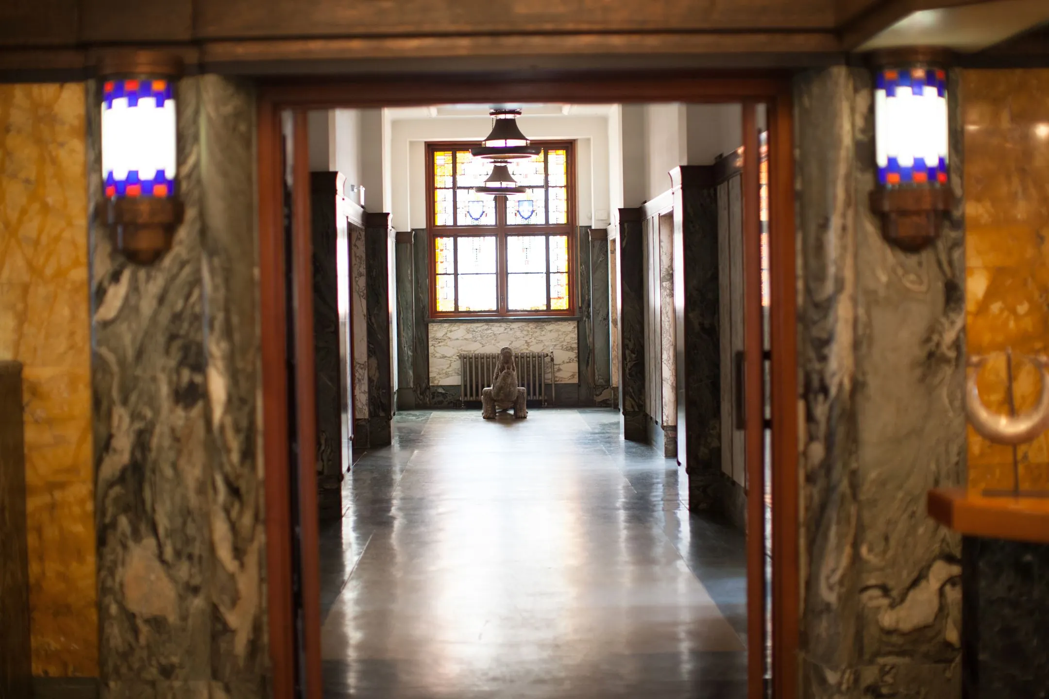 Marmeren gang in het gebouw aan de Ceresstraat 13 met een beeld en glas-in-loodraam aan het einde.