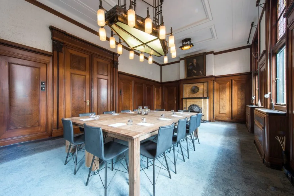 Vergaderruimte aan de Ceresstraat 13 met houten wandpanelen, een grote tafel en een opvallende hanglamp.