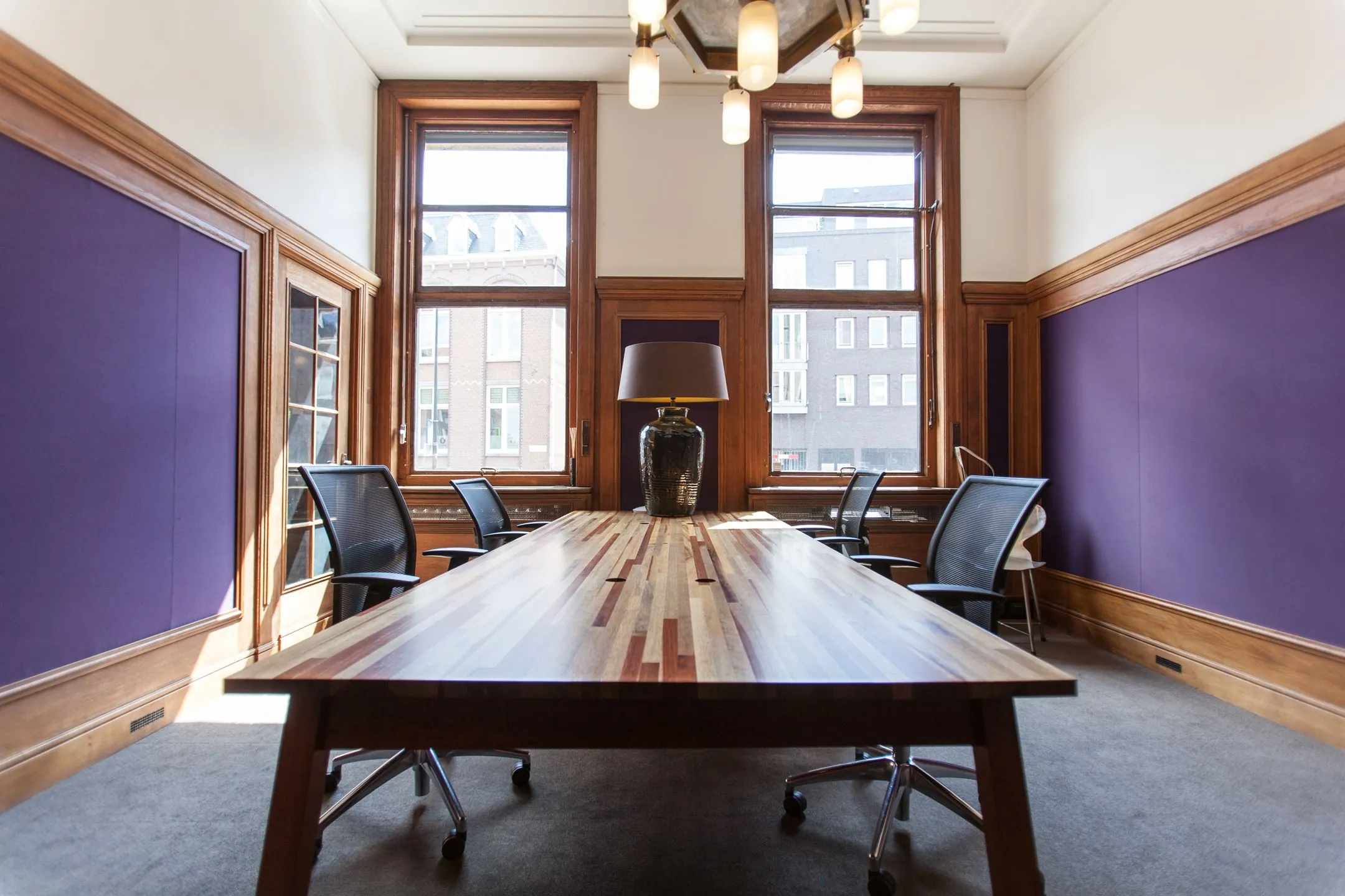 Vergaderruimte aan de Ceresstraat 13 met een houten tafel, paarse wandpanelen en grote ramen.