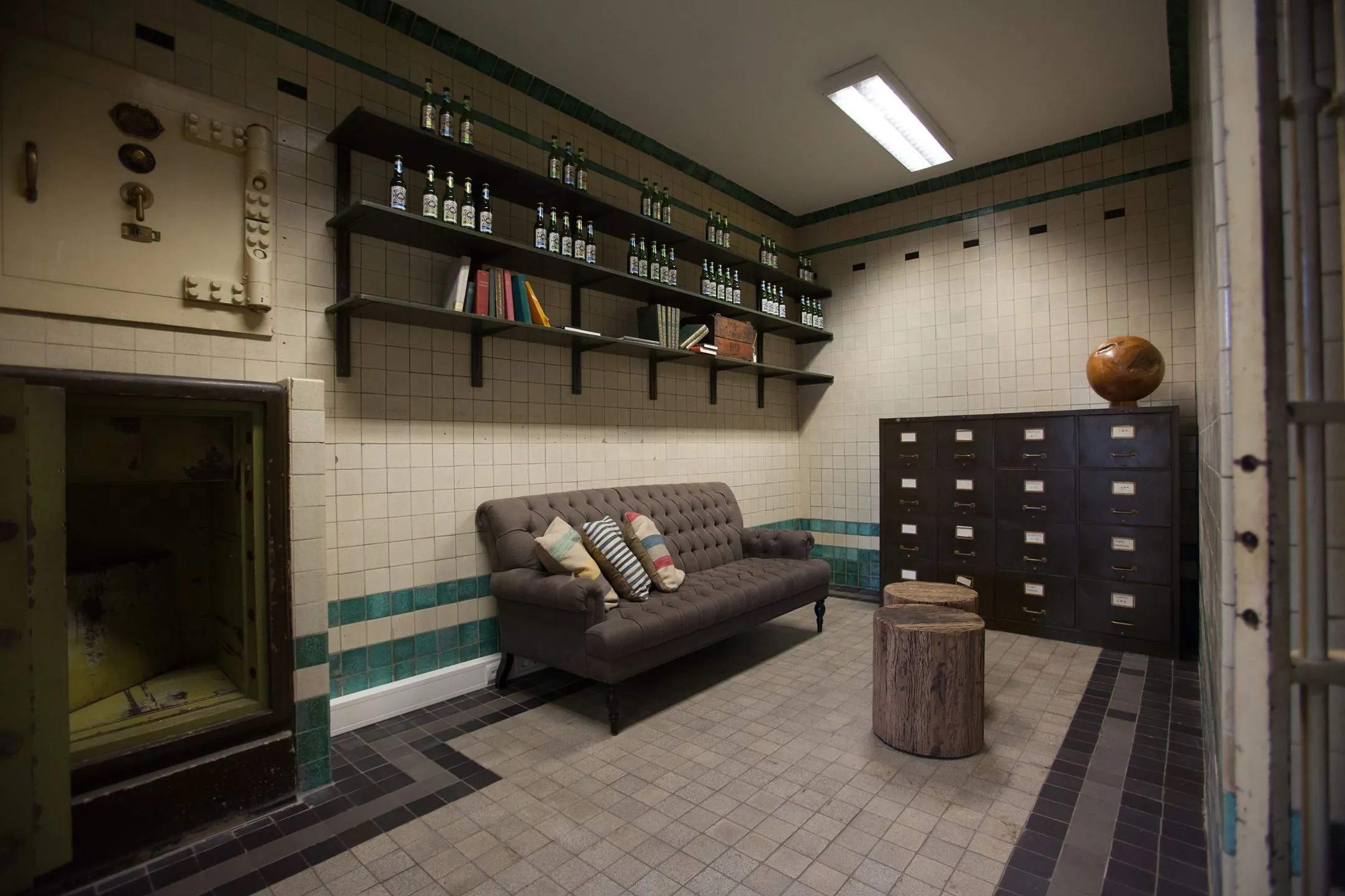 Industrieel ingerichte kamer met een vintage kluisdeur, bruine bank, houten krukjes en archiefkasten in Ceresstraat 13.