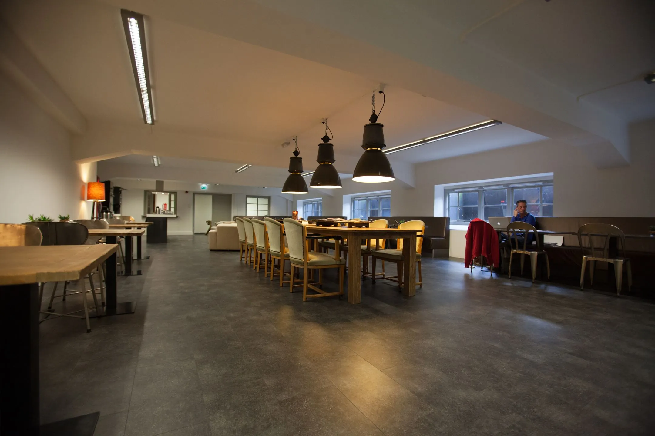 Ruime, modern ingerichte gemeenschappelijke ruimte met lange houten eettafel, zitplekken en industriële hanglampen in Ceresstraat 13.