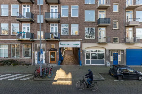 Voorgevel van een appartementencomplex aan de Coolhaven met een doorgang naar Agrolab Group Verwey, enkele geparkeerde fietsen en een passerende fietser.