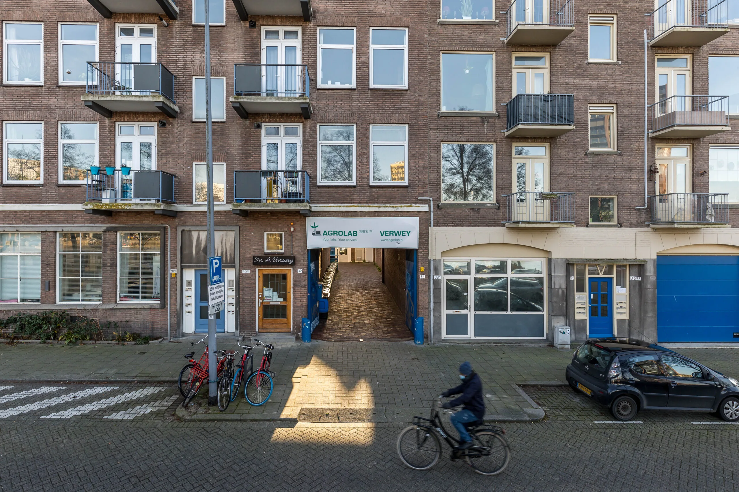 Voorgevel van een appartementencomplex aan de Coolhaven met een doorgang naar Agrolab Group Verwey, enkele geparkeerde fietsen en een passerende fietser.