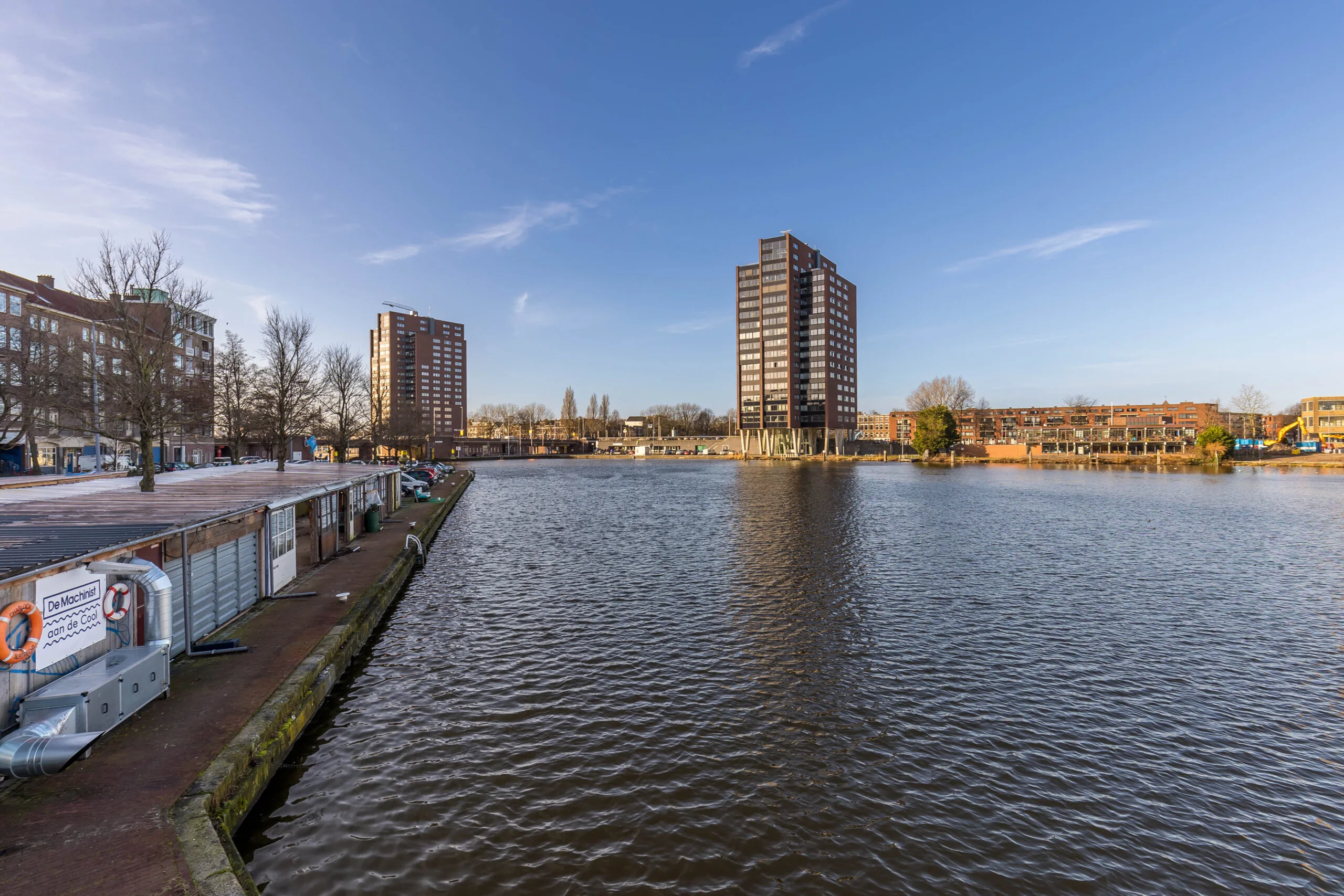 Uitzicht op de Coolhaven in Rotterdam met moderne hoogbouw en woonboten langs de kade op een zonnige dag.